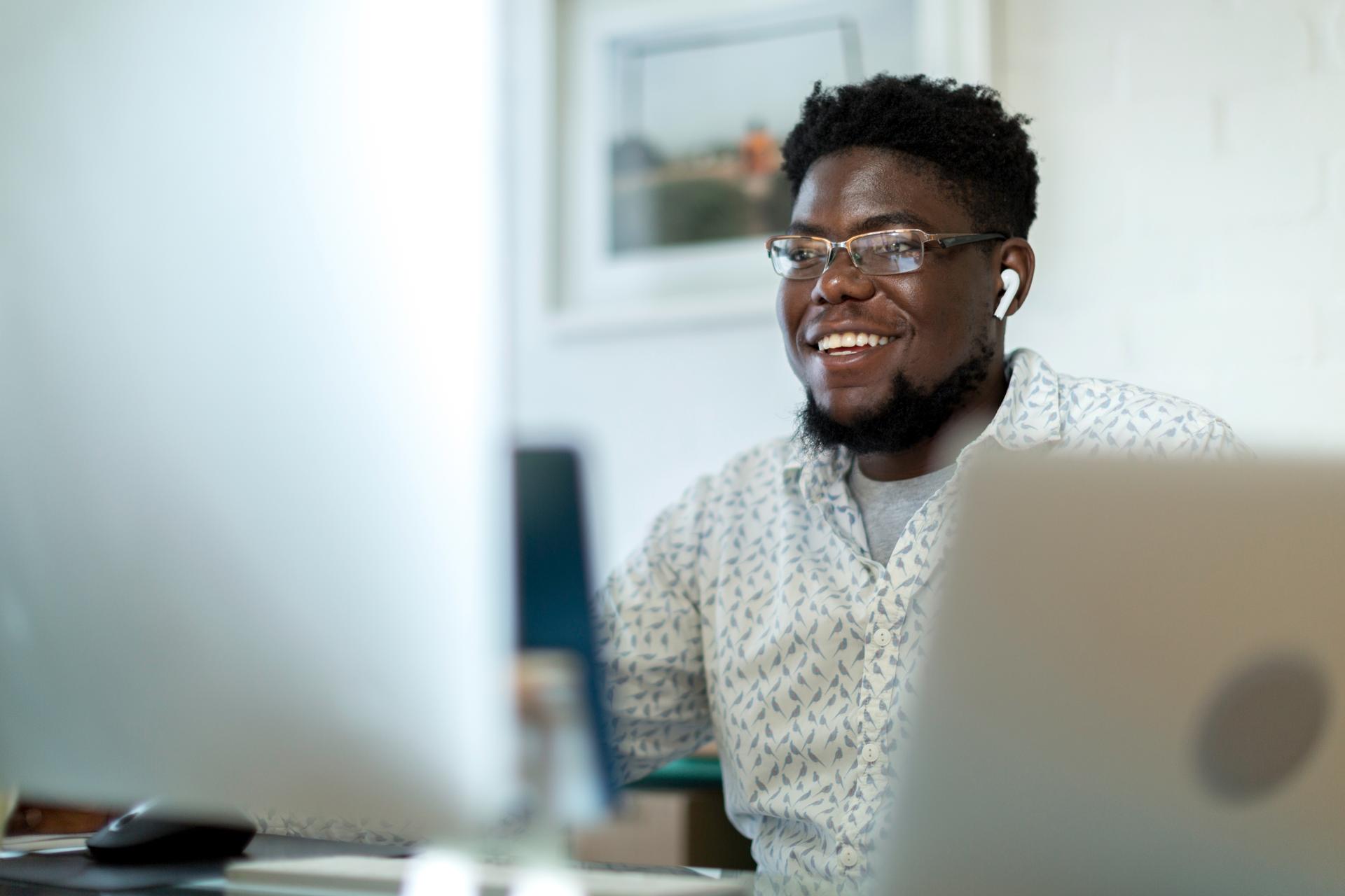 Young man with glasses and a beard looking at his desktop computer and smiling