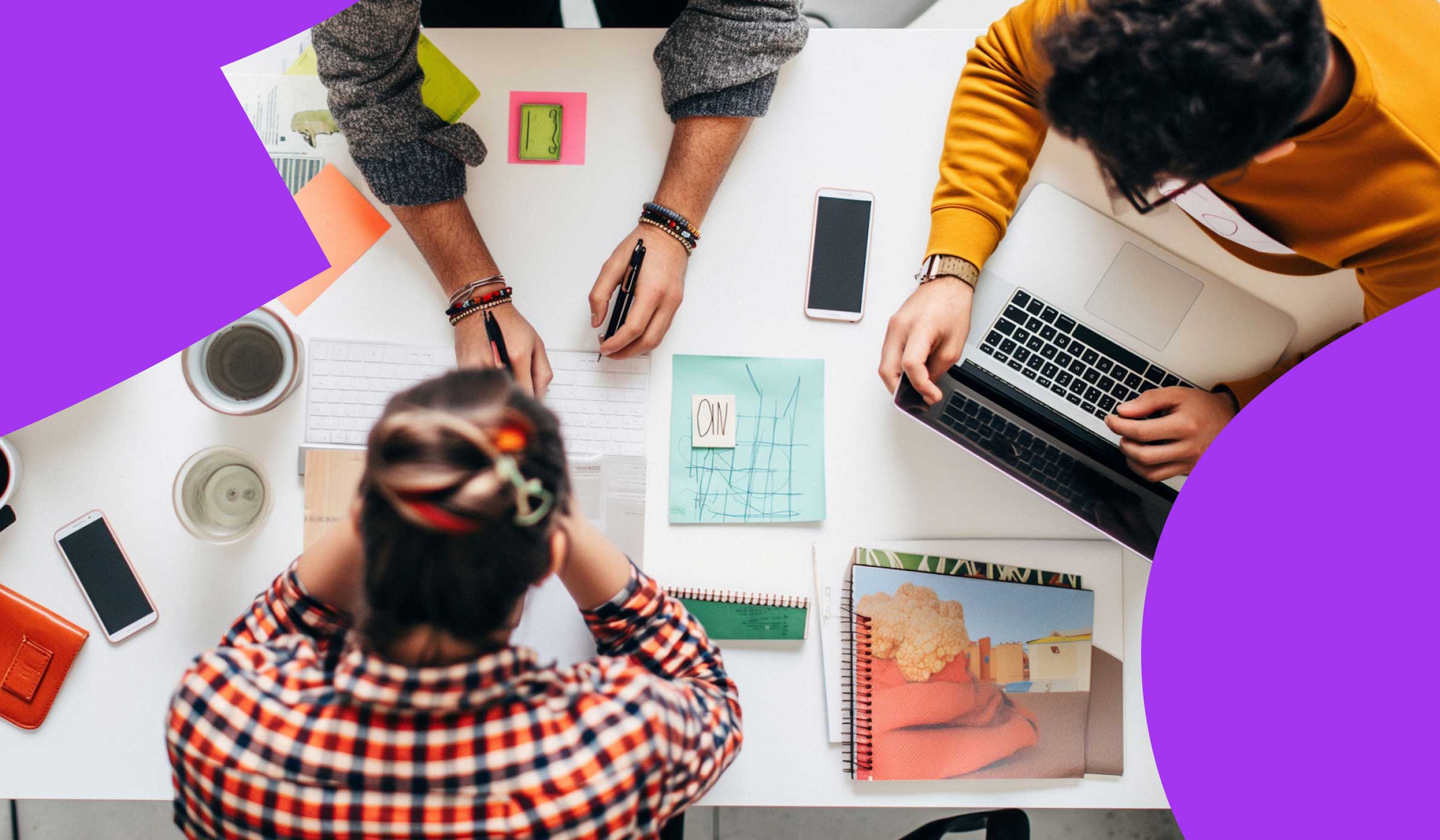 Overhead photo of a team of employees sitting in a conference room planning with notes and devices scattered across the table